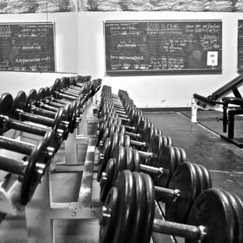 A long rack of dumbbells beneath chalkboard workout boards
