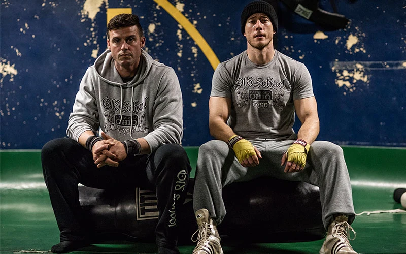 Two old-school gym owners sitting on a heavy bag in their gym